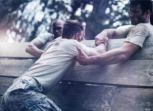 Soldiers helping one another over wall in obstical training