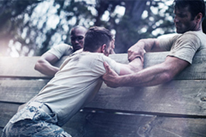 Soldiers helping one another over wall in obstical training