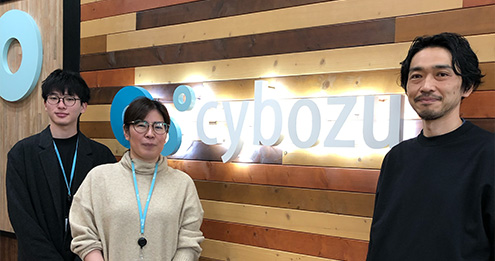 Three individuals standing in front of Cybozu sign