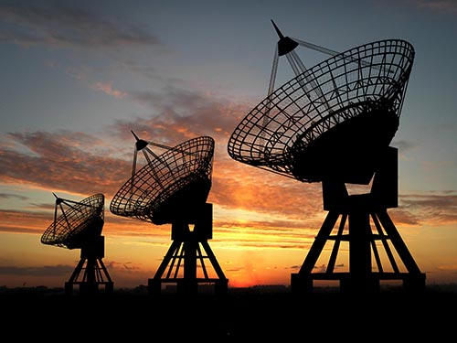 silouette of three satellites in front of a sunset