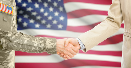 Two military personel shaking hands in front of the  American flag